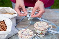 Step by step for creating hanging bird feeders out of teacups and yoghurt pots - tying on ribbons to suspend 