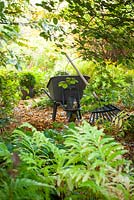 Wheelbarrow, rake and fallen leaves in the woodland area at Glebe Cottage