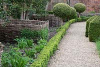 Topiary alongside gravel pathway with decorative compost bunkers - West Green House, Hampshire