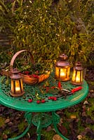 Garden table with Christmas lanterns and trug with mistletoe, rose hips, and holly