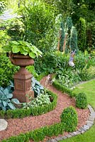 Gravel path edged with box, surrounded by mixed borders and urn with Hosta