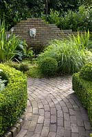 Brick pathway with clipped box hedges and wall mounted water feature