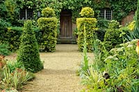 East Ruston Old Vicarage, East Ruston, near Norwich, UK. View to the front door from within Entrance Court. Clipped box cones and Ilex 'Golden King' topiary. 
