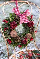Frosted wreath with berries and cones tied with ribbon to old metal chair