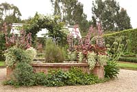 Glasshouse Garden with raised brick pond set in gravelled area with Beschorneria yuccoides, Miscanthus sinensis, Agapanthus and Rosa 'Marigold' on arch - East Ruston Old Vicarage  