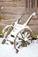 Old, wooden cart leaning against shed, covered in snow