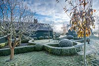 View to rear of house with wrought iron garden  seat. Yew and box topiary and dwarf hedges on frosty morning in December - The Mill House, Little Sampford, Essex