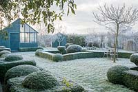 View to garden store and lean to greenhouse. Wrought iron garden table and seats. Yew and box topiary and dwarf hedges on frosty morning in December - The Mill House, Little Sampford, Essex