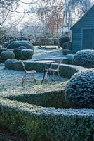 Wrought iron garden table and seats. Yew and box topiary and dwarf hedges on frosty morning in December - The Mill House, Little Sampford, Essex