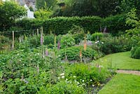 View of carefully managed country garden with flower filled borders merging in to vegetable garden with raised beds
