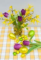 Flower arrangement of forsythia and purple tulips with foil wrapped easter eggs