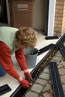 Woman clearing fallen dead leaves from guttering channel at garage entrance