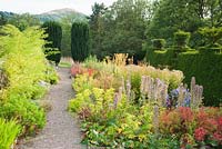 Path beside border of late summer perennials including Asters with Euphorbia and Phlomis, leads toward a pair of fastigiate yews framing a view to the British Camp, or Herefordshire Beacon - Perrycroft, Upper Colwall, Herefordshire, UK