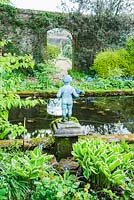 Pond garden planted with acers, ferns and hostas around a formal pool, with putto. Wayford Manor, Wayford, Crewkerne, Somerset, UK