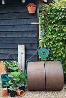 Old cast iron roller leaning against the barn with pots, watering cans and Hornbeam hedge - Woodpeckers