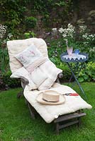 Day bed piled with cushions, with drinks table, straw hat and secaturs in small cottage garden - Garden Neighbours