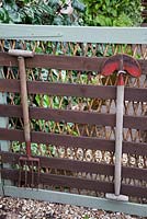 Painted wooden gate decorated with vintage garden tools, leading to vegetable garden. Garden Neighbours
