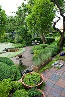 View over garden with planting of Antennaria dioica, Apple and Plum trees, Buxus topiary, Artemisia 'Silver queen', Brunnera, Lavender, Veronica spicata, Anaphalis, Vinca minor, Stachys lanata and Acaena. Terracotta tile and brick surfaces - Ulla Molin