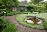Circular pond surrounded by planting of Antennaria dioica, Apple and Plum trees, Buxus and Taxus topiary, Artemisia 'Silver queen', Brunnera, Lavender, Veronica spicata, Anaphalis, Vinca minor, Stachys lanata, Acaena and Iris - Ulla Molin