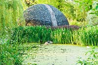 Dome structure constructed using empty bottles viewed over pond - Westonbury Mill 
 