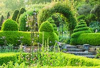 Formal courtyard garden on the west side of the house features Box hedging, metal obelisks supporting Clematis and flowers such as Irises, self seeded Aquilegias, Thalictrums and Peonies with steps leading up to Rose and Clematis arches - The Old Rectory