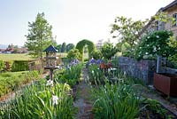 Bird table, stone wall, rest area with bistro garden furniture and a clipped hornbeam arch in a terraced country garden with Iris germanica and Paeonia suffruticosa 'Kouka Mon' 