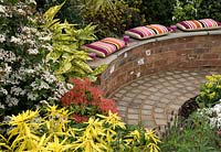 Circular paved area with seating and backdrop of colourful and contrasting shrubs including Aucuba japonica Crotonifolia, Viburnum tinus, Pieris and Choisya 'Aztec Gold' - 'At the End of the Day' Show Garden, Silver Gilt Award, Harrogate Spring Flower Show 2013