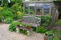Lean-to greenhouse with wooden seat, stone effect bench, container flowers and vegetables.