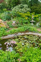 Large pond surrounded with densely planted perennials and container plants