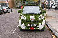 Front of car covered in artificial grass advertising the company supplying the product with a face picked out in white grass at the front, street in Marylebone, London