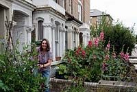 Naomi Schillinger, author of Street Veg, working in her front garden in Finsbury Park with sweet peas - Lathyrus odoratus - in front and Hollyhock - Alcea -  in the next door garden, London Borough of Islington, UK