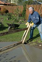 Man using home made levelling device for screeding concrete in the base of a garden DIY project