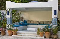 Outdoor living area with pots planted with Chamerops humilis 'Cerifera', Pelargonium and Epidendrum 