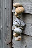 Pebbles with holes hanging from string against a wooden shed