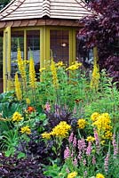 Yellow painted summerhouse with yellow Ligularia and pink Lythrum. The Water garden. RHS Tatton Park Flower show 2013