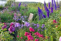 Wooden bench in border planted with Phlox paniculata 'Lilac Time', Phlox paniculata 'Grenadine Dream', Rosa and Delphinium 'Pagan Purples'
