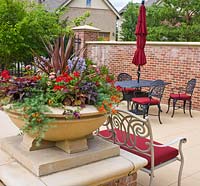 Small patio area with container planted with Cordyline 'Red Sensation', Ipomoea, Verbena, Nemesia, Petunia, Lantana, Salvia and Lotus 