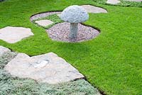 Stepping stone path across lawn and Thymus pseudolanuginosus with decorative stone mushroom in circular gravel bed in 'Reflections of Japan'. Gold medal winner at RHS Tatton Flower Show 2013