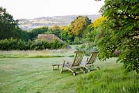 Wooden deckchairs on lawn overlooking summer borders and Sussex countryside