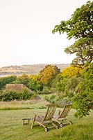Wooden deckchairs on lawn overlooking summer borders and Sussex countryside 