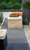 Metal floorgrate and wooden box as seat with orange and brown pillows. Buxus balls in border