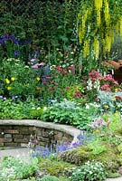 Raised border of colourful perennials surrounding patio