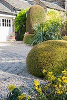 Clipped yew spheres frame the drive and the circular maze formed of stone setts laid in to the gravel with gate into garden beyond. 