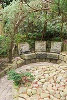 Stone seats below a larch arbour with oval detailing set into the paving
