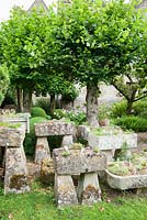 The Troughery, a collection of stone troughs collected from around the farm, planted with alpines. Behind them are pleached limes in the Winter Garden. Rodmarton Manor, Rodmarton, Tetbury, Glos, 