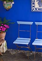 Small town garden - Courtyard with cobalt blue walls, blue cafe chairs and ceramic picture from Portugal, ceramic container and terracotta pot.