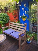 Decked area with colourfully painted feature walls and seating area.  Small town garden, Brighton, UK 