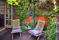 Deck chairs on wooden decked patio outside house in walled small town garden with Fuchsia, Pyracantha, Brighton, UK 
