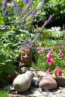 Sculpture of human head in terracotta and vase on the granite stone path within Petunia hybrida 'F1 Parure' and Salvia transsylvanica