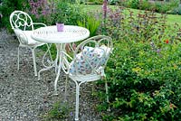 Ornamental white metal table and chairs on gravelled area of cottage garden 